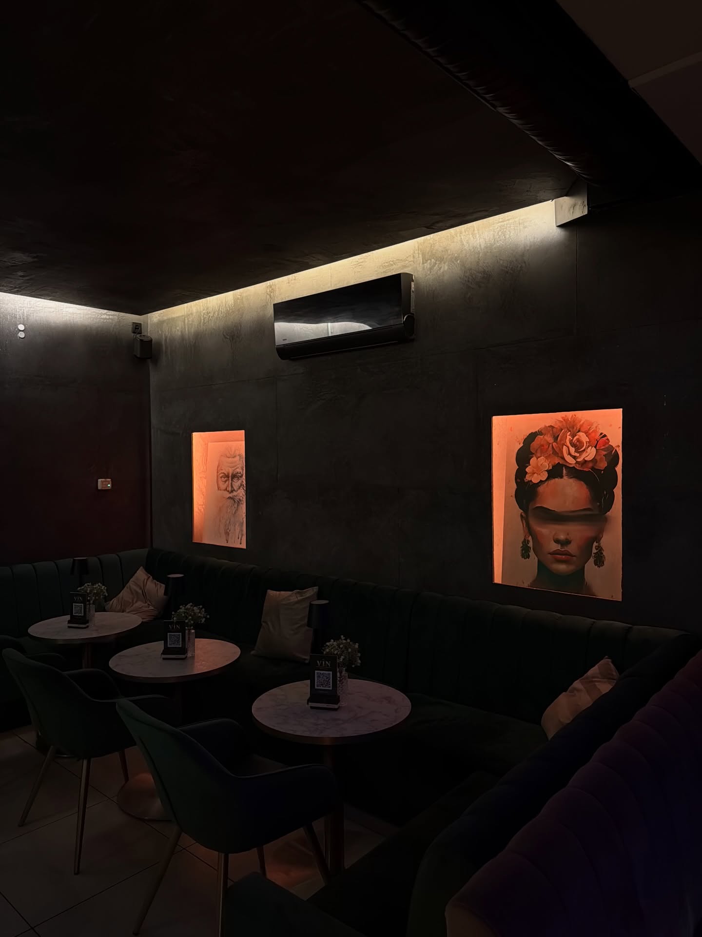 Lounge mit dunklen Wänden, beleuchteten Bildern und runden Marmortischen
